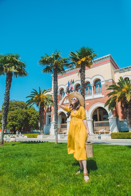 Mujer con vestido amarillo con sombrero de paja con bolsa en las palmeras de la calle con un edificio antiguo en el fondo