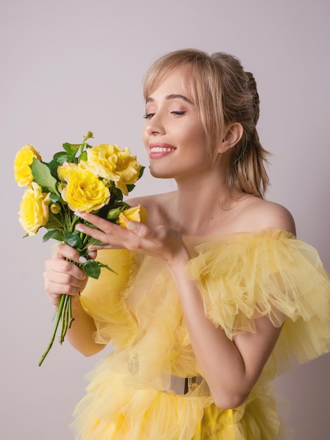 Una mujer con un vestido amarillo sostiene un ramo de flores.