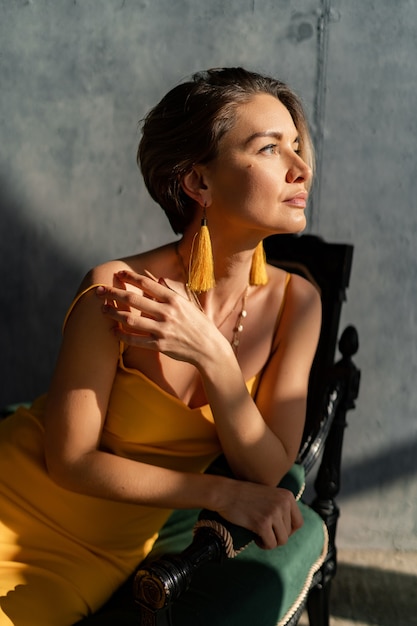 Mujer en vestido amarillo de verano con peinado corto en el interior de la habitación muro de hormigón posando