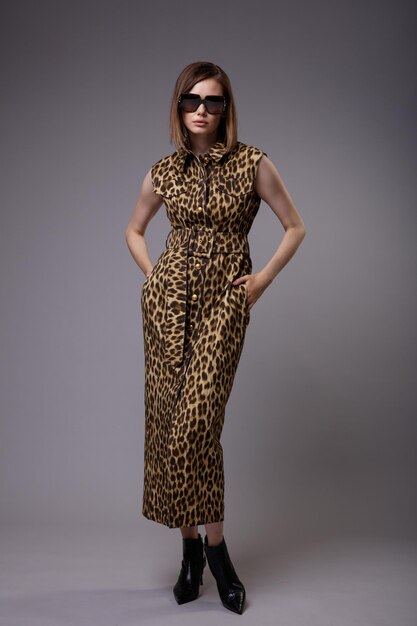 Mujer en vestido animal leopardo botines negros gafas de sol sobre fondo gris figura delgada