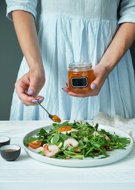 Mujer con un vestido azul agrega salsa a un plato con ensalada. concepto de cocina