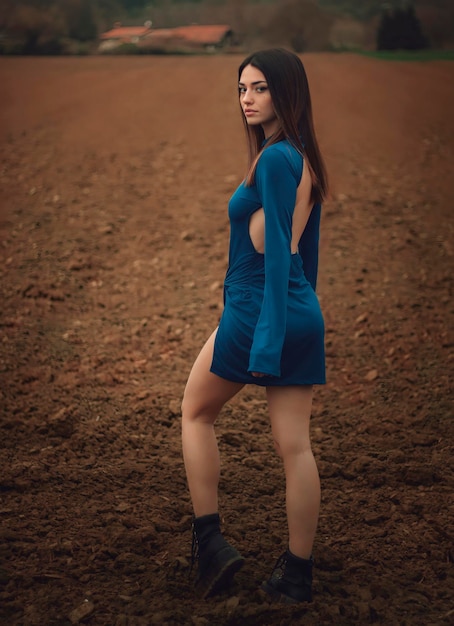 Una mujer con un vestido azul se para en un campo de espaldas a la cámara.