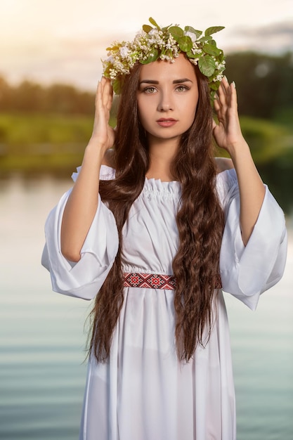 Mujer con vestido blanco en el agua. Arte Mujer con corona en la cabeza en el río. Corona en la cabeza, tradiciones eslavas y paganismo.