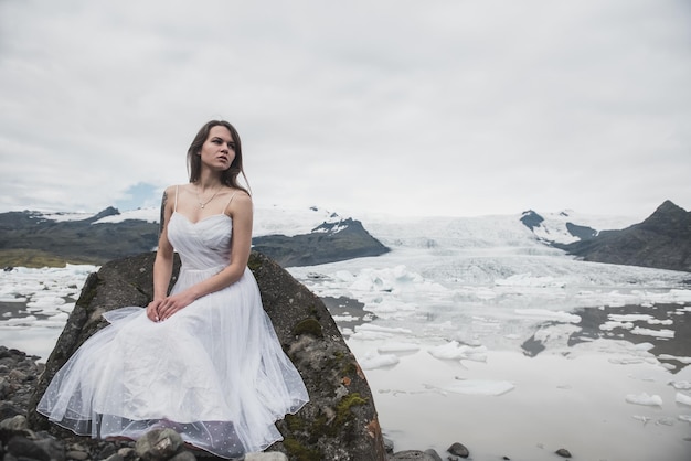 Mujer con vestido blanco se alza contra el fondo de los glaciares en Islandia