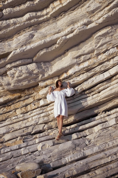 Mujer con vestido blanco apoyándose en la repisa de la roca al estilo de las manipulaciones corporales juguetonas arrugadas arrugadas lente gran angular