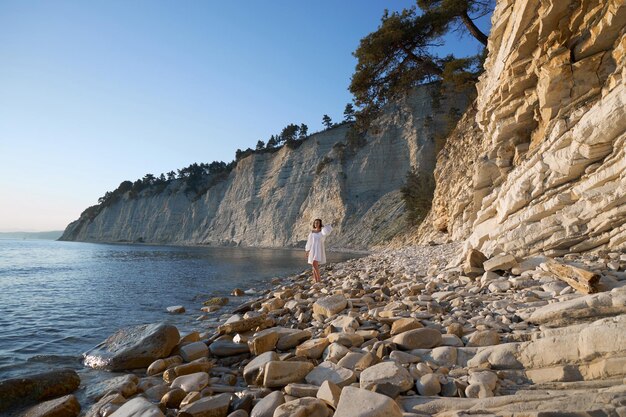 Mujer con vestido blanco caminando cerca de la orilla en el borde del acantilado