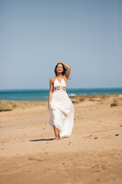 Mujer en vestido blanco caminando de frente sobre la arena de la playa