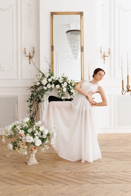 Mujer en vestido blanco cerca de flores en estudio clásico