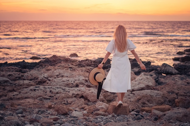 Mujer con vestido blanco disfrutando del hermoso atardecer de mar mientras viajaba a Chipre