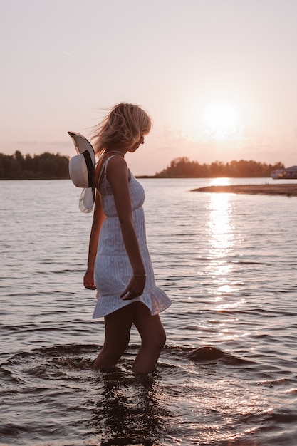 Una mujer con un vestido blanco en el fondo de la puesta de sol una hermosa joven rubia en un verano blanco ...