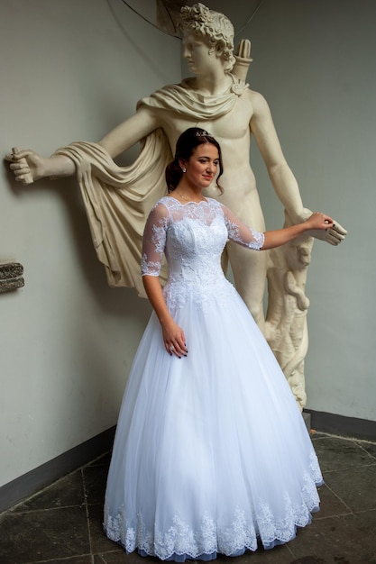 Una mujer con un vestido blanco se para frente a una estatua de una mujer con un vestido blanco.