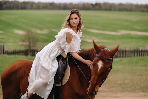 Una mujer con un vestido blanco montando a caballo en un campo