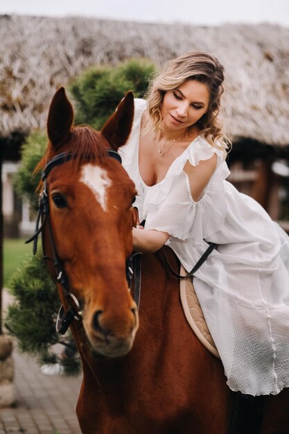 Una mujer con un vestido blanco montando un caballo cerca de una granja