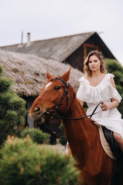 Una mujer con un vestido blanco montando un caballo cerca de una granja