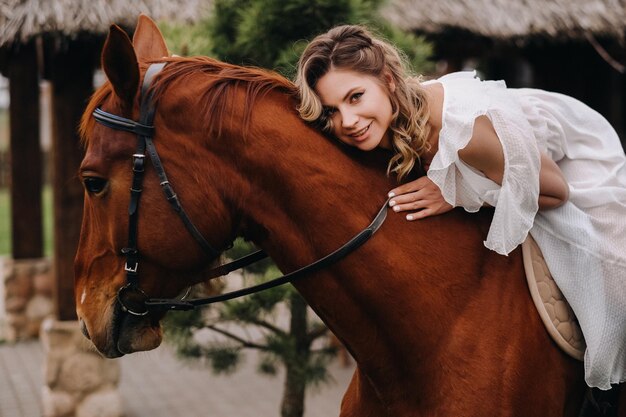 Una mujer con un vestido blanco montando un caballo cerca de una granja