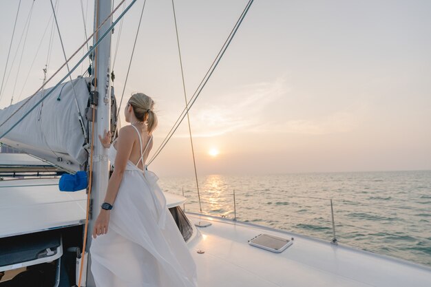 Mujer con vestido blanco relajarse en yate de vela, puesta de sol romántica