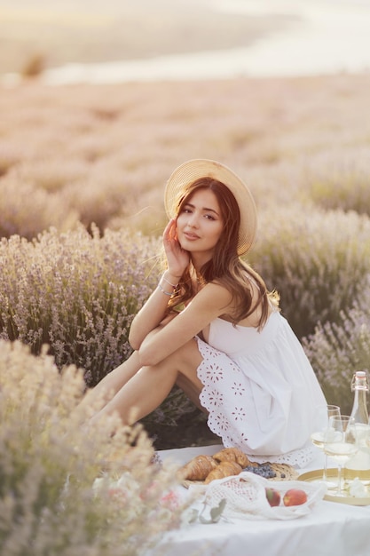 Una mujer con un vestido blanco se sienta en una manta de picnic en un campo de lavanda