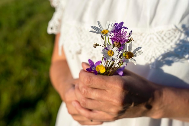 Mujer con un vestido blanco sostiene un ramo de flores silvestres en sus manos