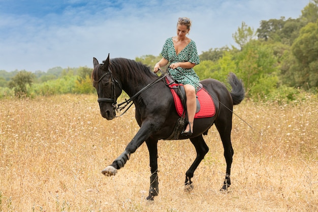 Mujer con un vestido con un caballo negro en la naturaleza