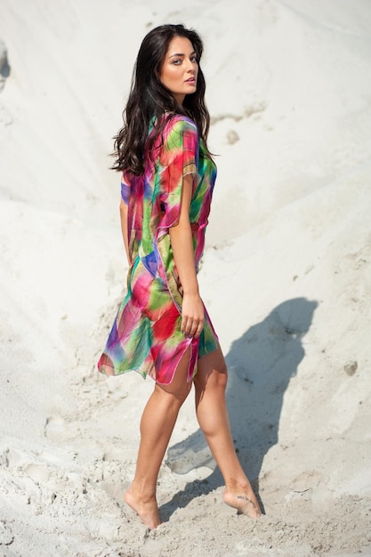 Una mujer con un vestido colorido se para en la arena.