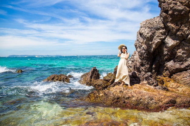 Mujer en un vestido crema está de pie, disfrutando del hermoso mar en la playa.