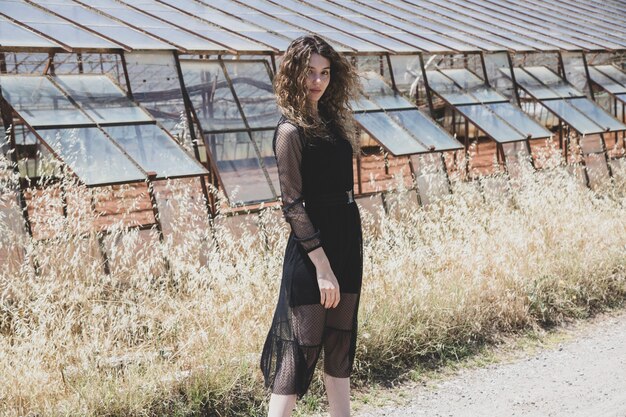 mujer en un vestido de encaje negro posando cerca del invernadero