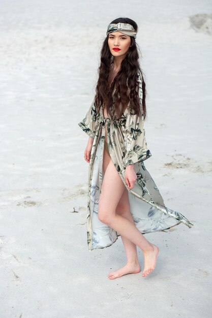 Una mujer con un vestido con una falda larga y un sombrero está de pie en la playa.