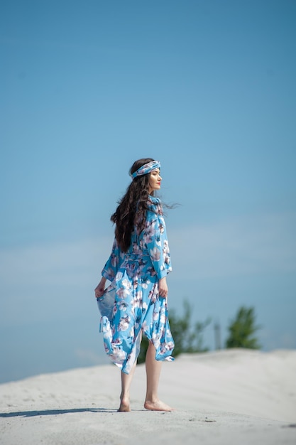 Una mujer con un vestido floral azul camina sobre una colina con el cielo de fondo.