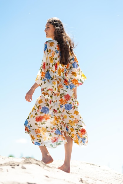 Una mujer con un vestido floral camina por la playa.