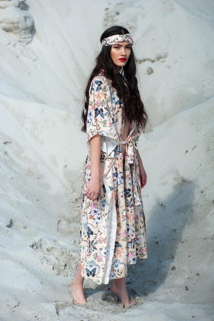 Una mujer con un vestido floral se para frente a una duna de arena.