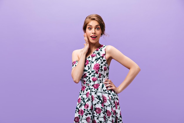 Mujer en vestido floral mirando sorprendida sobre fondo púrpura Moderna dama maravillosa en traje de verano posando en cámara sobre fondo aislado