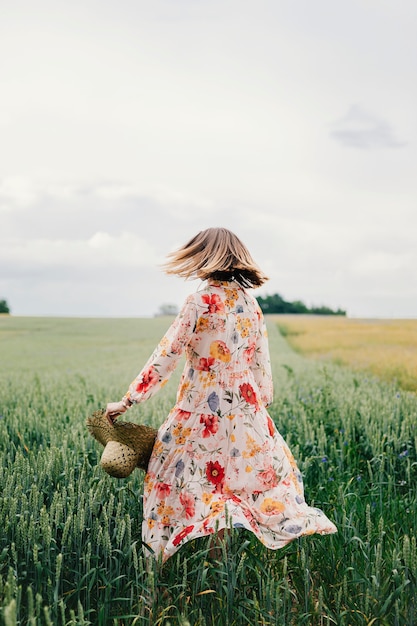 Mujer con un vestido floral con un sombrero tejido en un campo