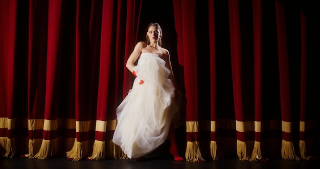 Mujer con un vestido fluido en un escenario con cortinas rojas