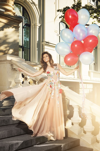 Mujer en vestido hermoso con muchos globos de colores