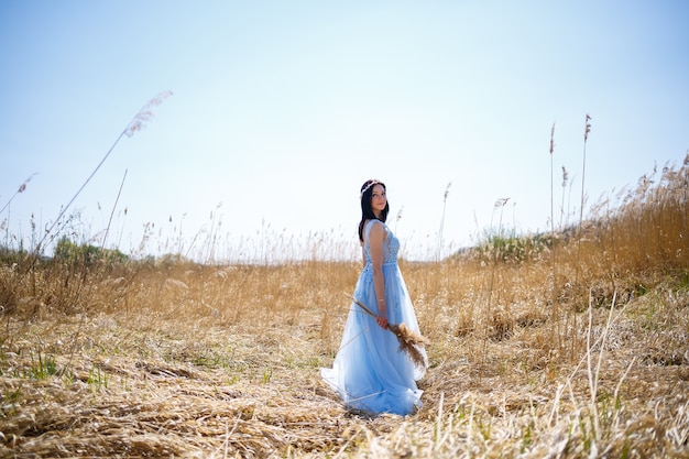 Mujer con un vestido largo azul en las cañas. Retrato de moda con flores secas