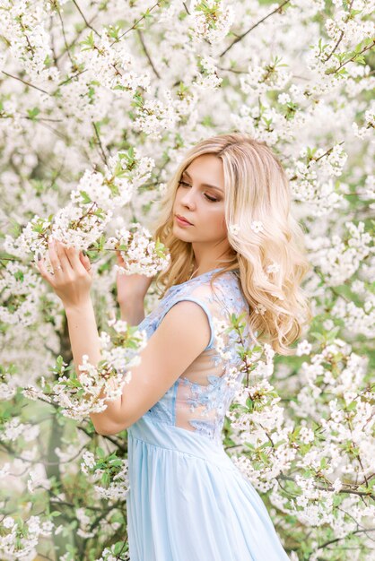 Mujer con un vestido largo azul en un jardín de primavera. Foto tierna con flores blancas