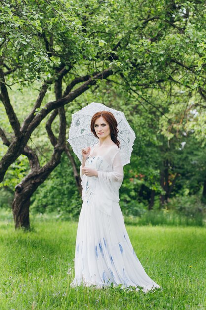 Mujer con vestido largo y blanco en el jardín de verano