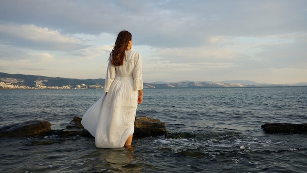 Mujer con vestido largo blanco y de pie en la playa