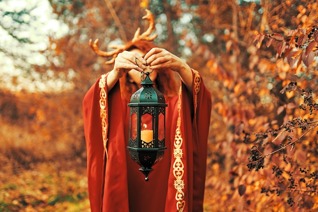 Mujer en vestido largo rojo con cuernos de ciervo en el bosque de otoño.