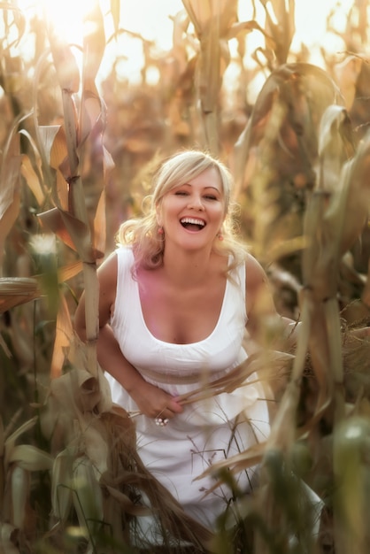 Mujer con un vestido largo de verano blanco camina sobre un campo de maíz y posando en el atardecer.