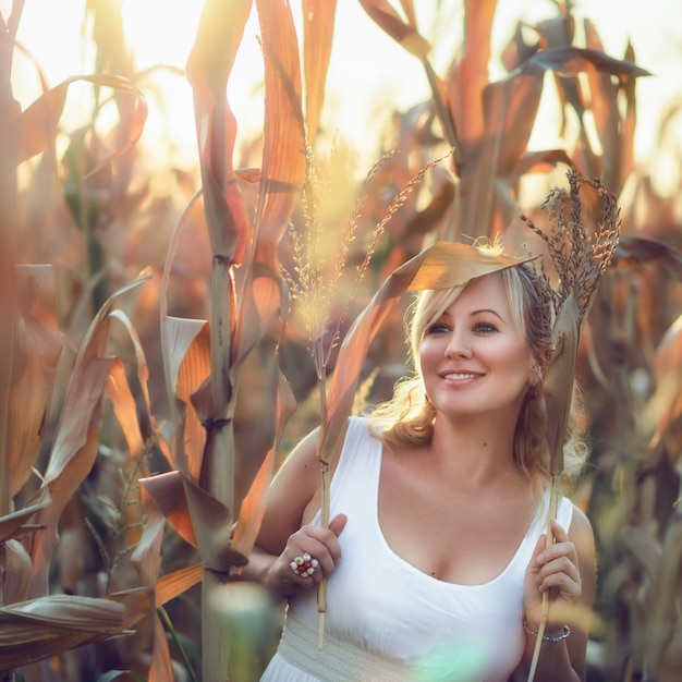 Mujer con un vestido largo de verano blanco camina sobre un campo de maíz y posando en el atardecer.