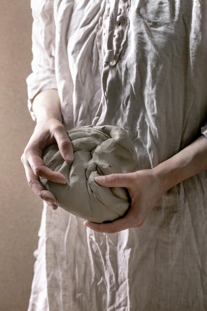 Mujer en vestido de lino sostenga pieza de arcilla gris cruda bricolaje cerámica cerámica hobby