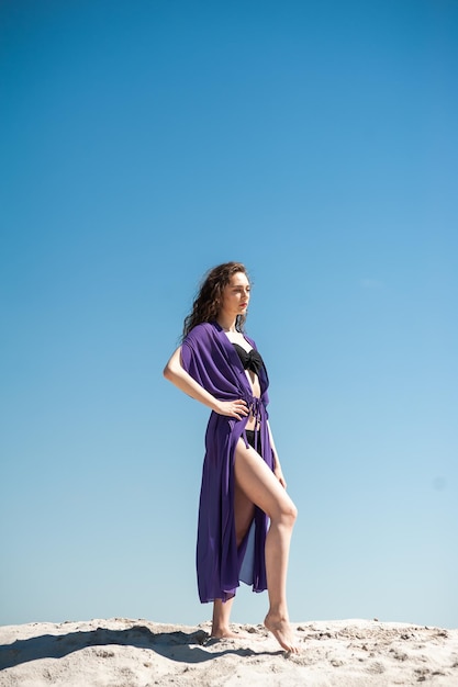 Una mujer con un vestido morado se encuentra en una playa.