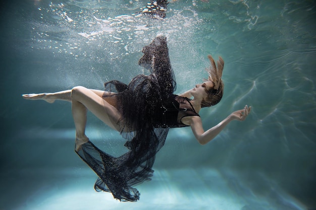 Mujer con un vestido negro para nadar bajo el agua como en un cuento de hadas