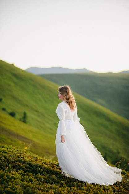 Mujer en un vestido de novia corre por el campo hacia las montañas