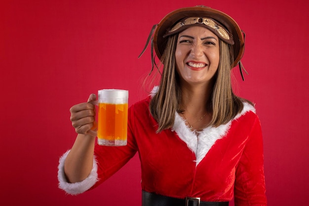 Mujer con un vestido de Papá Noel, un sombrero brasileño del noreste y un vaso de cerveza sobre un fondo rojo