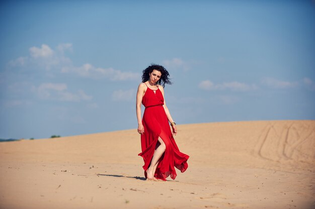 Mujer en vestido rojo bailando en el desierto en el cielo azul