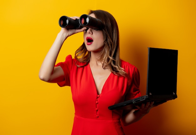 mujer en vestido rojo con binoculares y computadora portátil