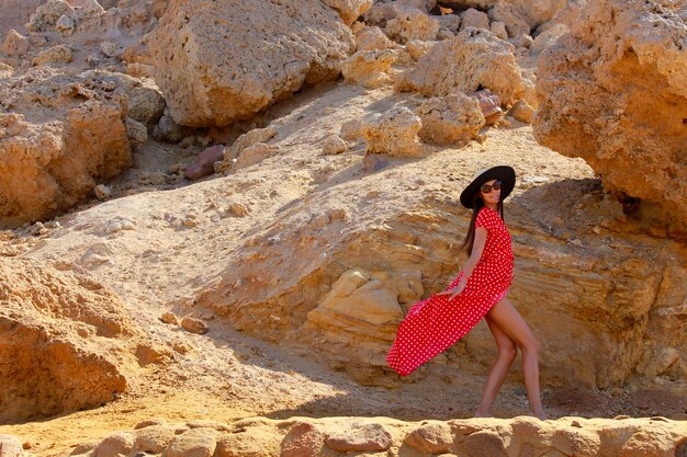 Foto una mujer con un vestido rojo está caminando por una playa rocosa