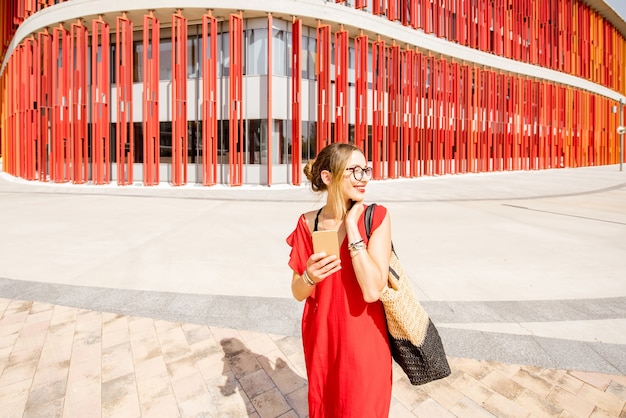 Mujer en vestido rojo caminando sobre el fondo de la pared del edificio moderno. Planta general con composición geométrica abstracta